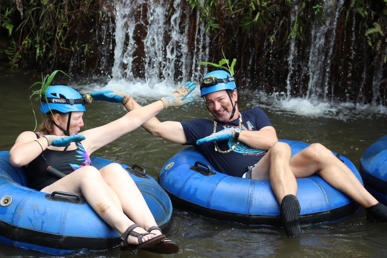 Two people in helmets and gloves enjoying river tubing near a small waterfall.