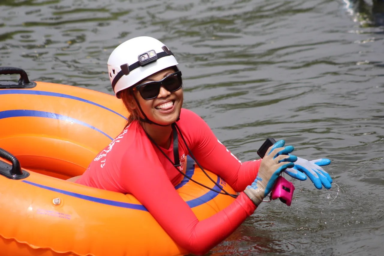 Person in helmet and gloves smiling in an orange inner tube on water.