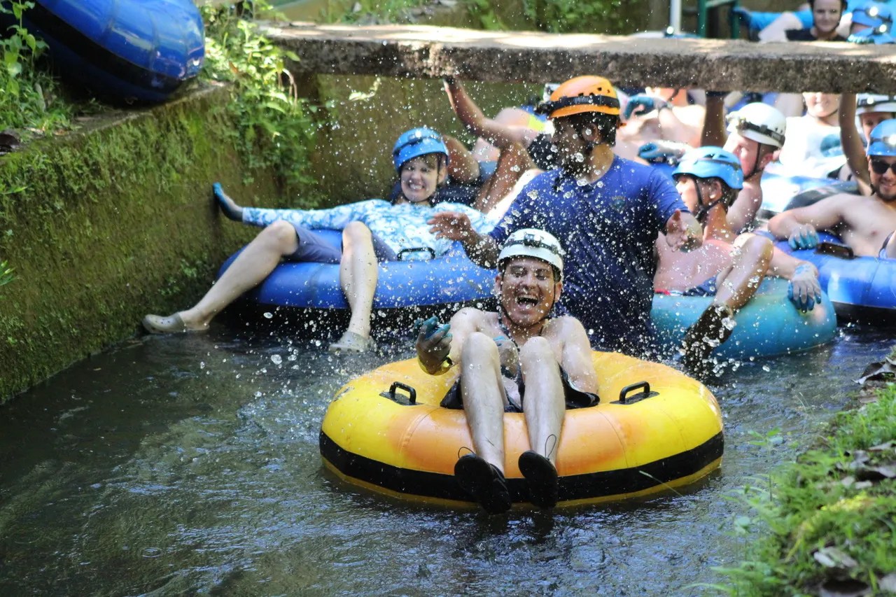 People tubing down a water channel, wearing helmets and life vests, splashing water around.