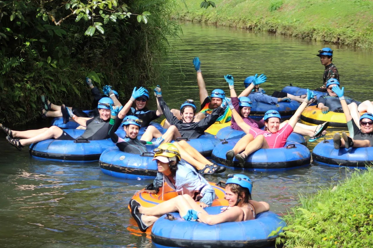 Group of people wearing helmets and gloves, tubing down a narrow river.