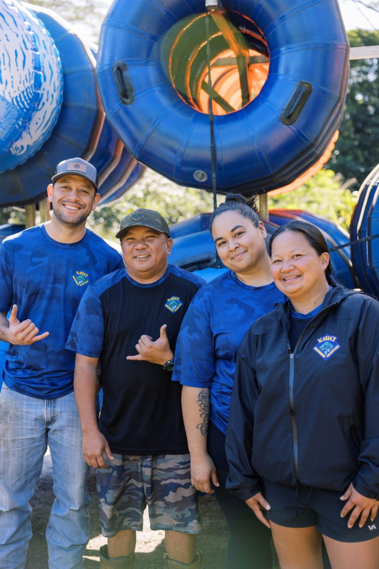 Four people smiling in front of stacked blue tubes outdoors.