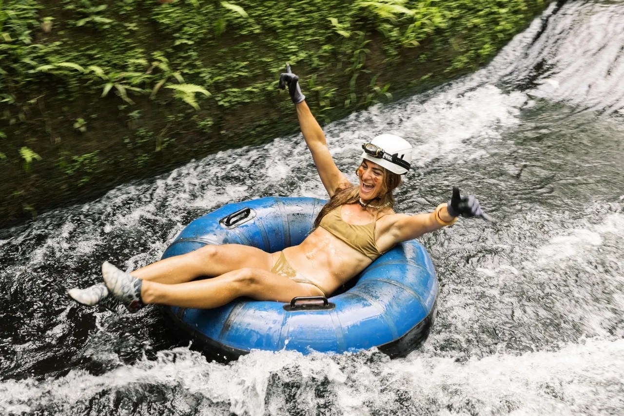 Person in helmet tubing down a river, arms raised in excitement.