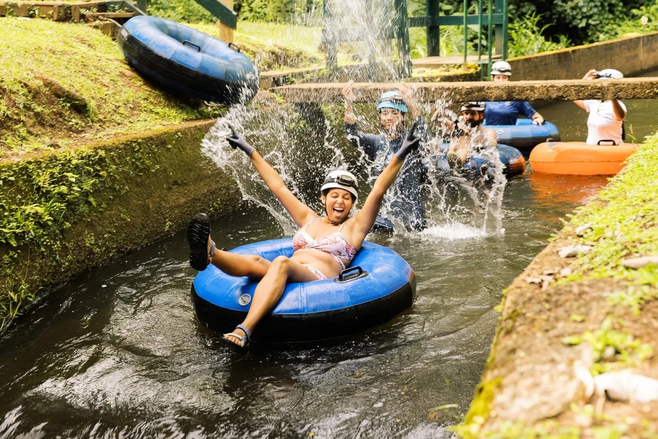 People in helmets tubing down a water slide, one person smiling with arms up.
