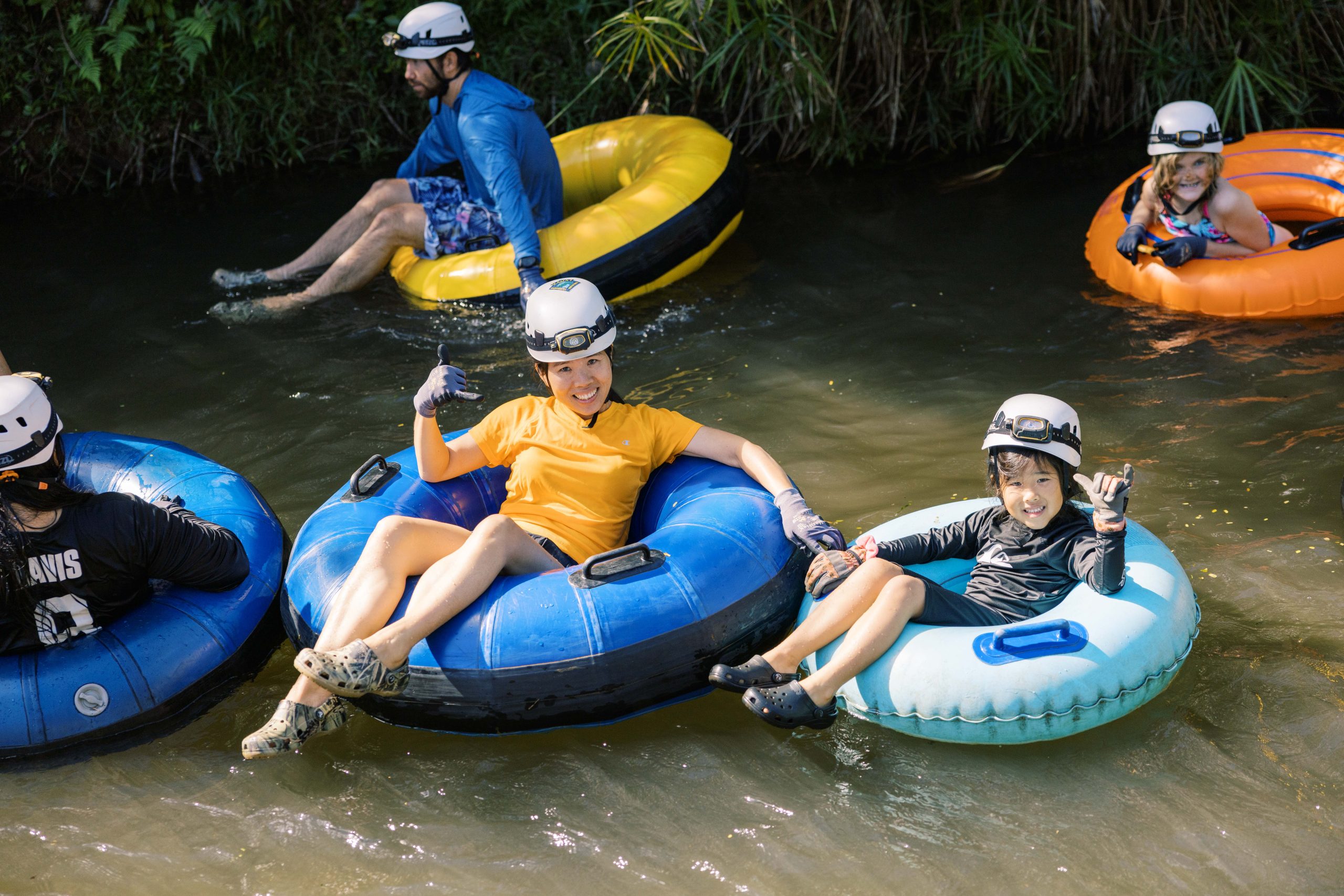 People tubing on a river, wearing helmets and life vests.