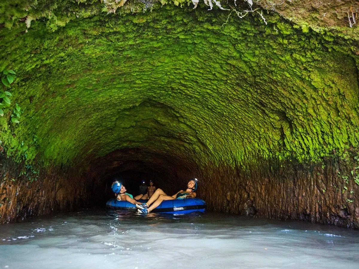 Two people on inflatable tubes in a mossy cave tunnel.