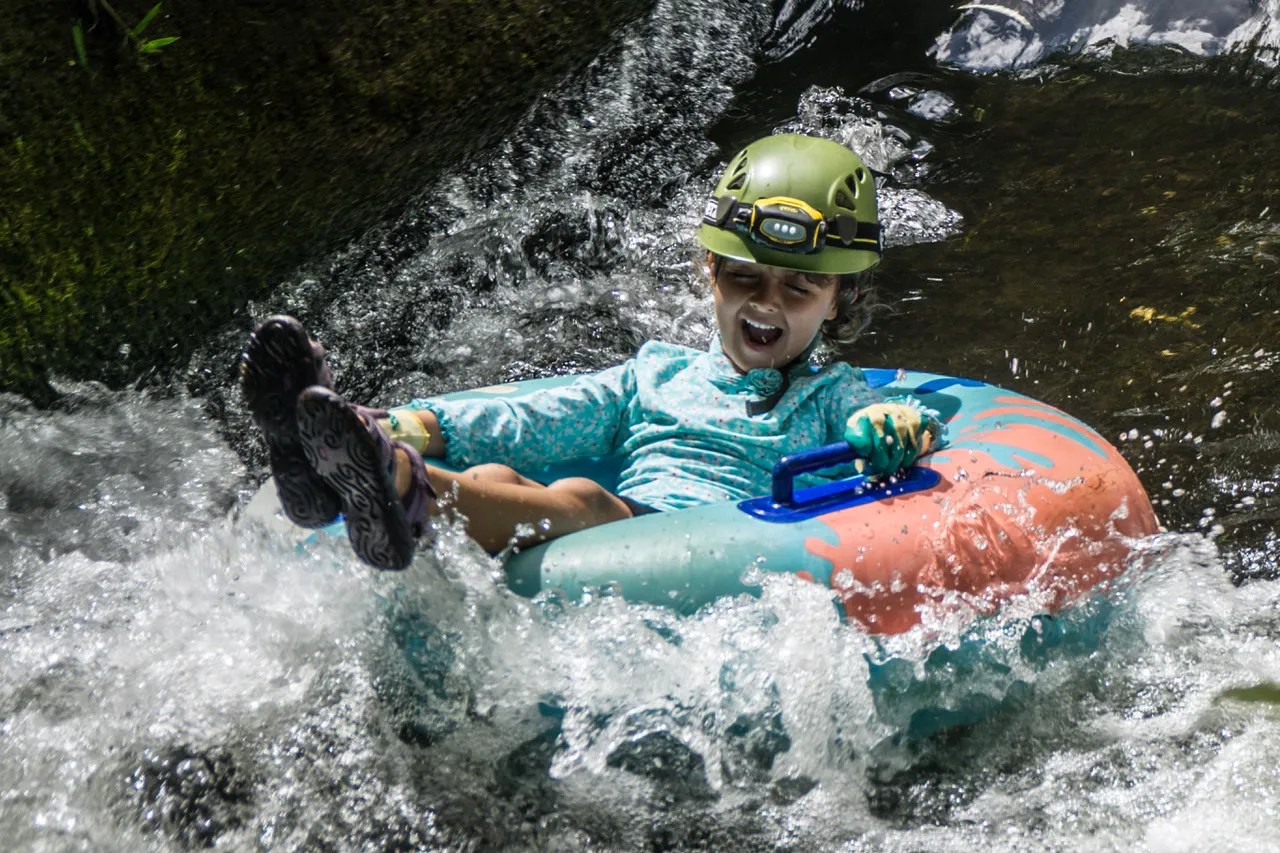 Child tubing down a river, wearing a helmet and water shoes, in an inflatable ring.