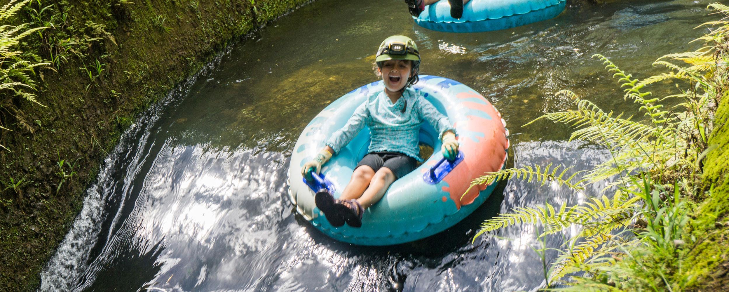 Child tubing down a narrow water channel with a joyful expression.