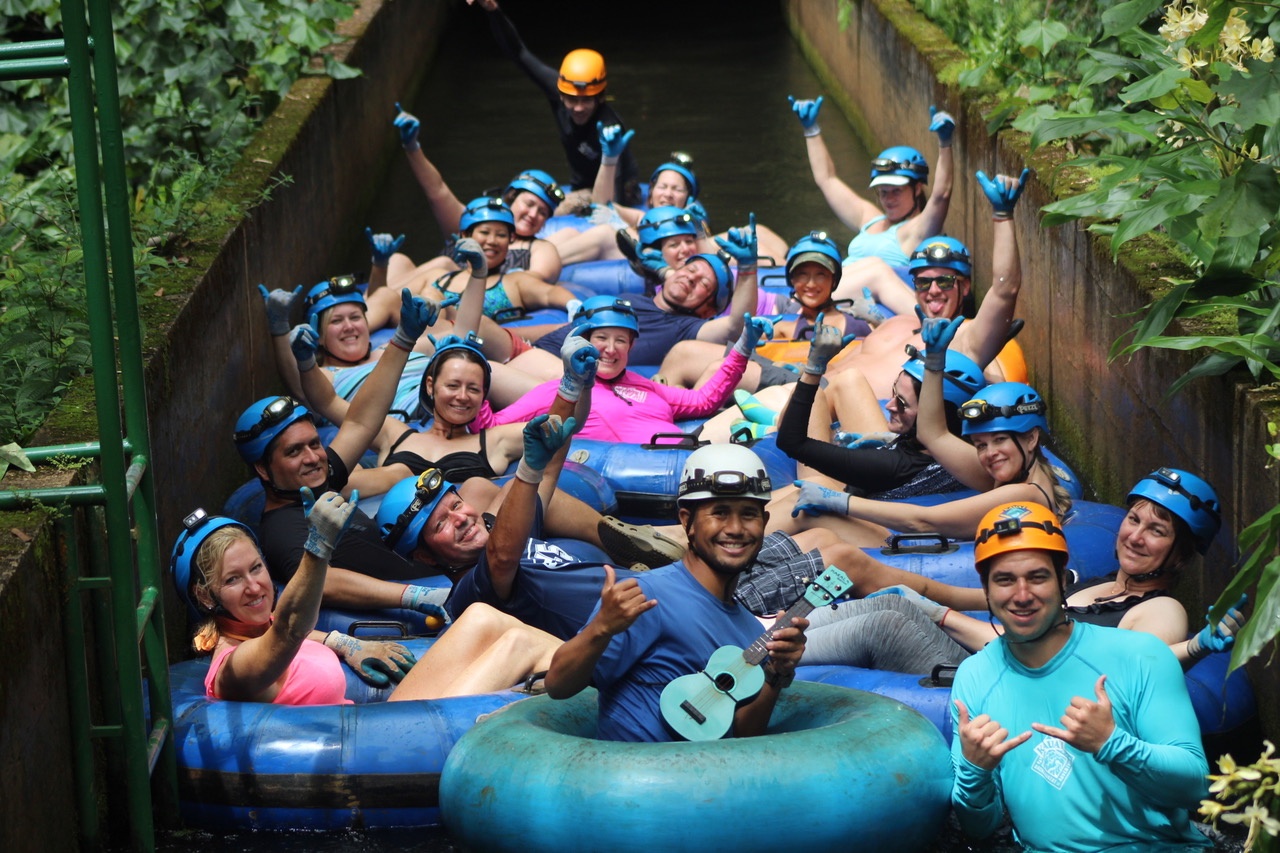 Group of people in helmets and life vests posing on inflatable tubes in a water slide.