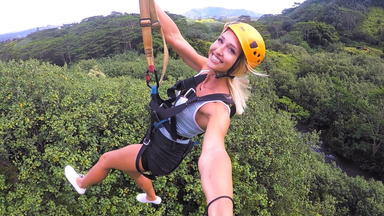 Woman ziplining over a lush green forest, wearing a yellow helmet.