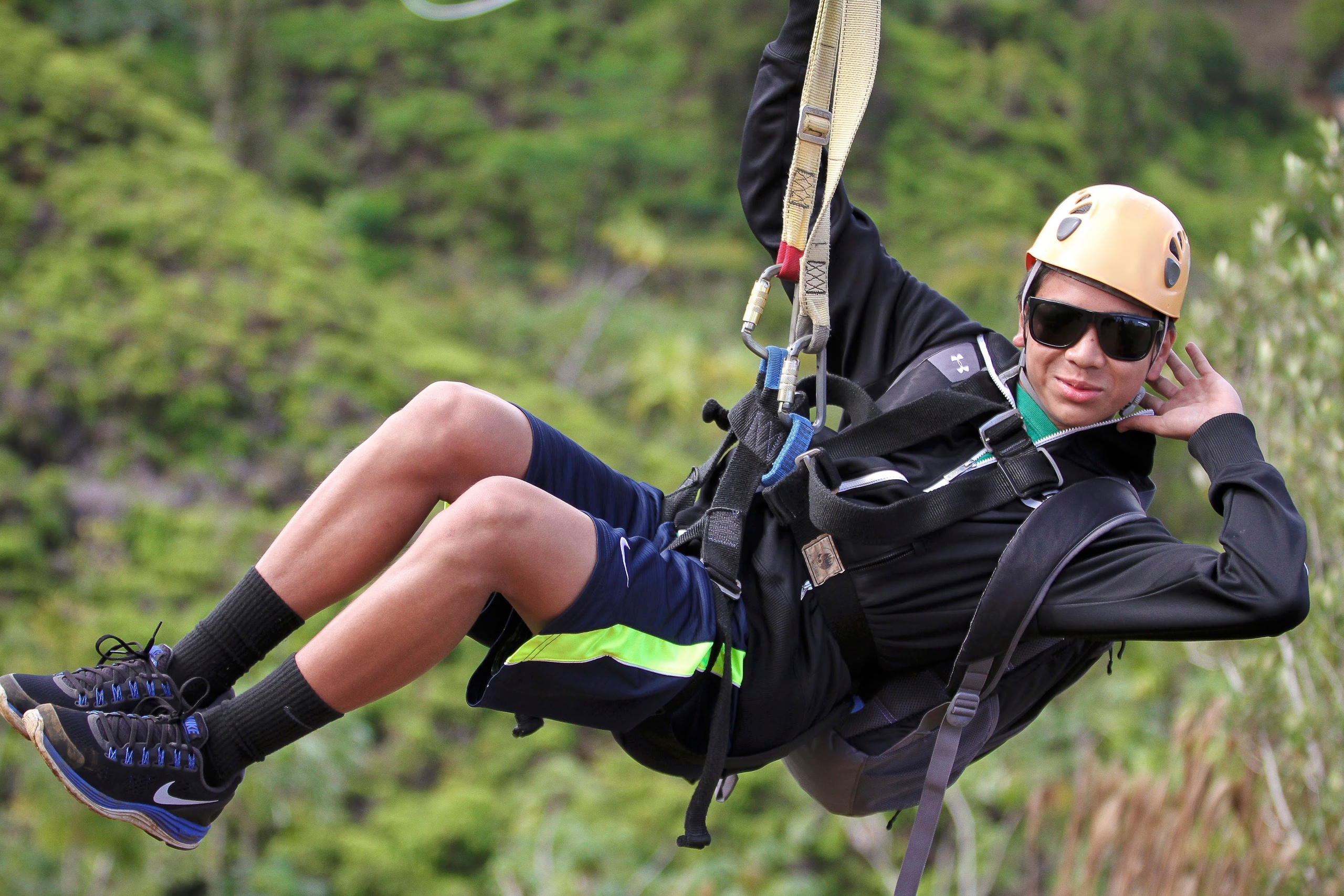 Person zip-lining in outdoor setting, wearing helmet and sunglasses.