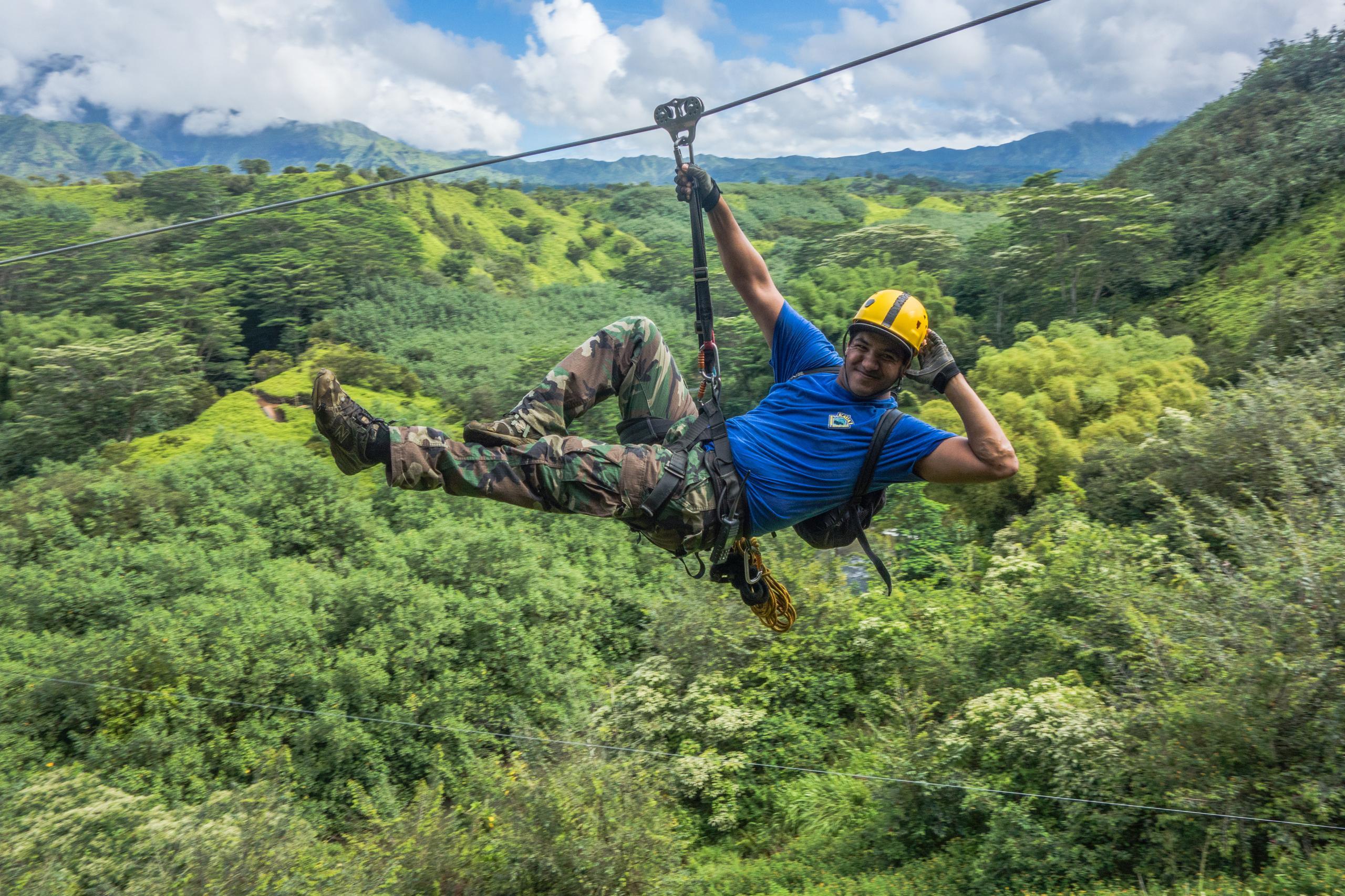 Person ziplining over lush green forest.
