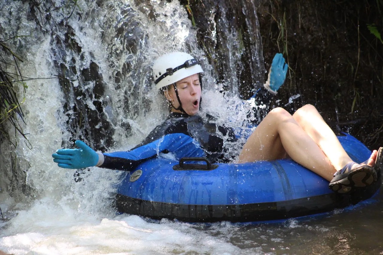 Person in helmet and gloves tubing down a waterfall