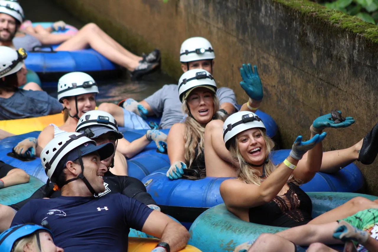 Group of people in helmets tubing in a water canal, smiling and enjoying.
