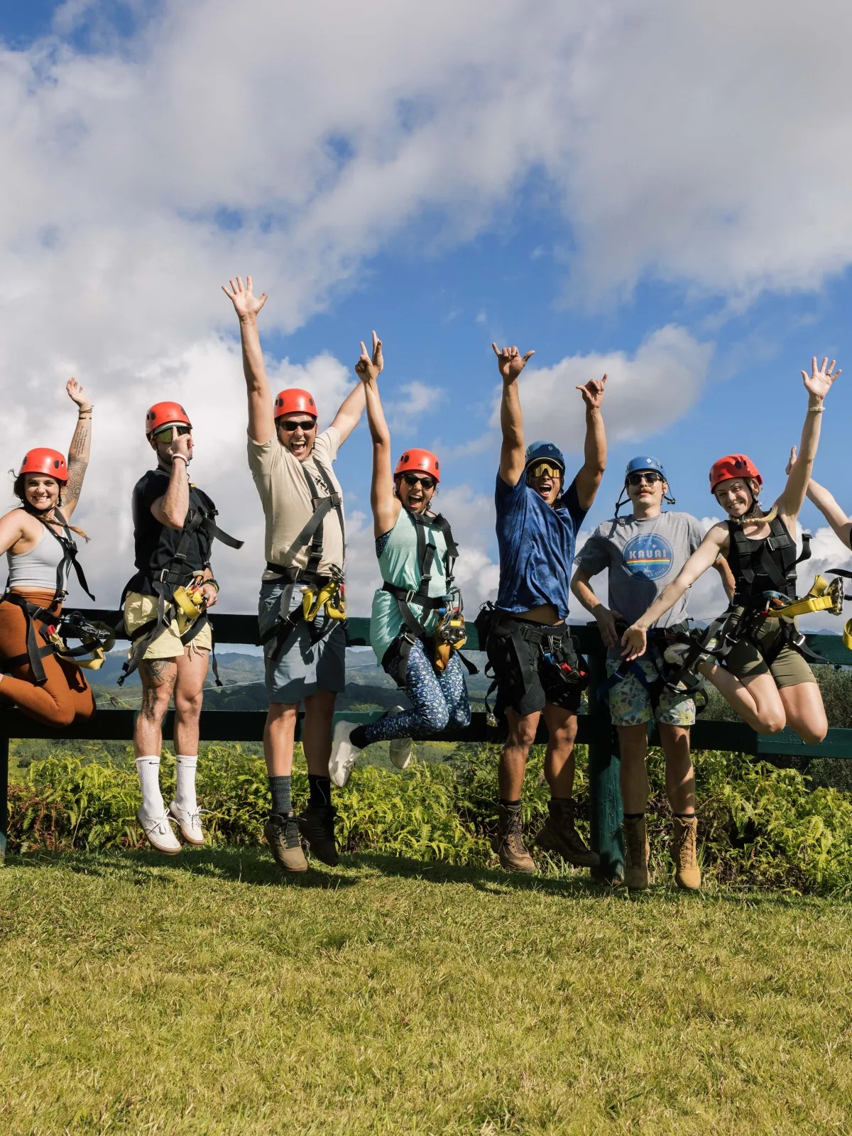 Group of people wearing helmets and harnesses joyfully jumping outdoors.