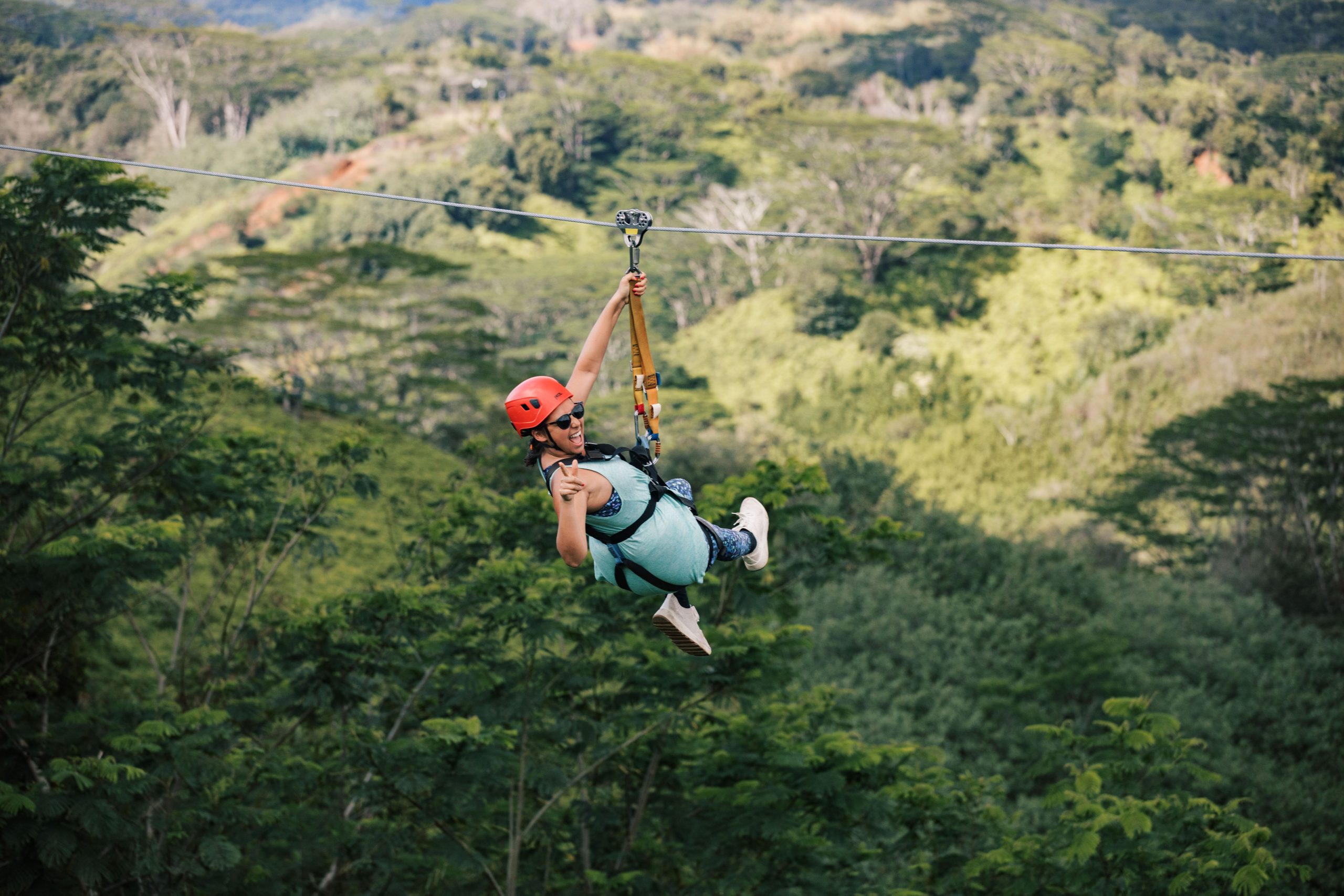 Person zip-lining through lush green forest with a helmet and harness.
