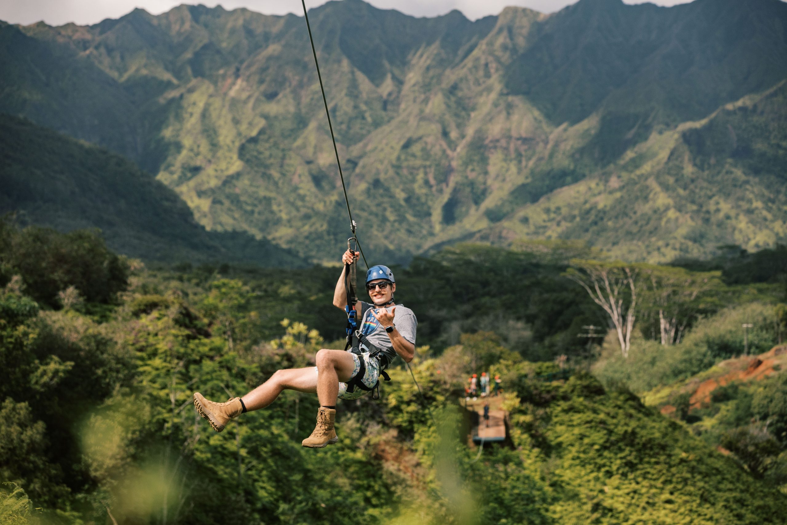Person ziplining over lush green valley with mountains in background.