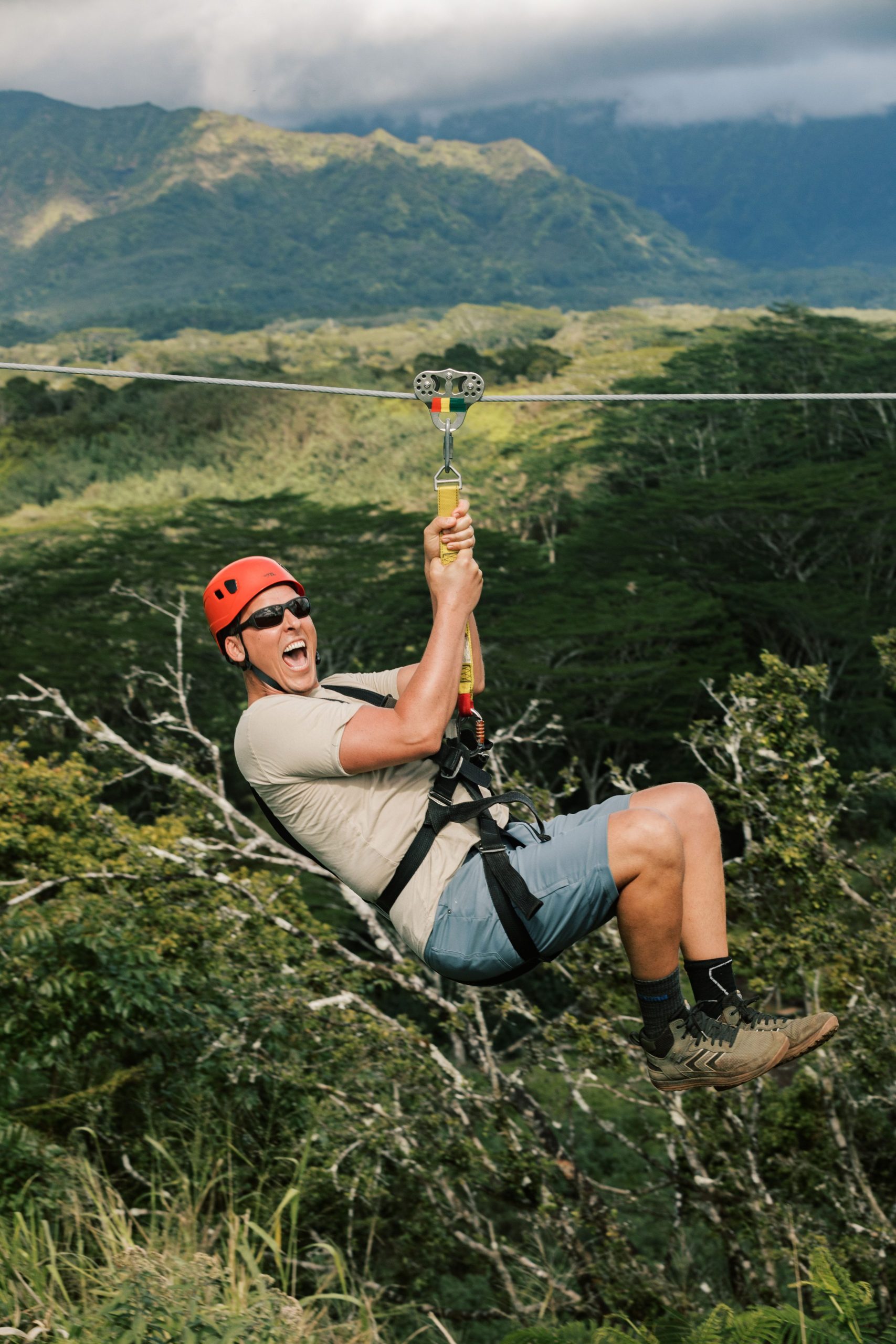 Person ziplining over lush green landscape with mountains in the background.