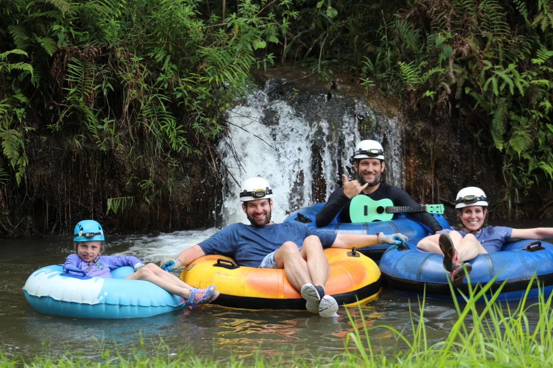 Four people in helmets tubing on a stream near a small waterfall.